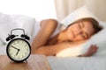 Beautiful young woman sleeping and smiling while lying in bed comfortably and blissfully on the background of alarm Royalty Free Stock Photo