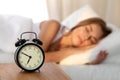 Beautiful young woman sleeping and smiling while lying in bed comfortably and blissfully on the background of alarm Royalty Free Stock Photo