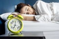 Beautiful young woman sleeping and smiling while lying in bed comfortably and blissfully on the background of alarm clock is going Royalty Free Stock Photo