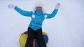 Beautiful young woman slides slide in snow on an inflatable snow tube and waves hand. Happy girl slides through snow on