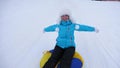 Beautiful young woman slides slide in snow on an inflatable snow tube and waves hand. Happy girl slides through snow on