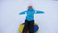 Beautiful young woman slides slide in snow on an inflatable snow tube and waves hand. Happy girl slides through snow on