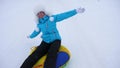 Beautiful young woman slides slide in snow on an inflatable snow tube and waves hand. Happy girl slides through snow on