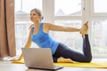 Beautiful young woman in sportswear doing sport exercises on yoga mat at home. Fitness training online with a laptop. Healthy Royalty Free Stock Photo