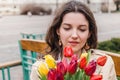 Beautiful young woman with spring tulips flowers bouquet at city street. Happy girl sitting on a bench outdoors. Spring portrait Royalty Free Stock Photo