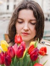 Beautiful young woman with spring tulips flowers bouquet at city street. Happy girl stay outdoors. Spring portrait of pretty Royalty Free Stock Photo