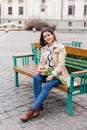 Beautiful young woman with spring tulips flowers bouquet at city street. Happy girl sitting on a bench outdoors. Spring portrait Royalty Free Stock Photo