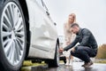 Young man helping charming woman to fix car wheel. Royalty Free Stock Photo