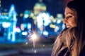 Beautiful young woman standing and holding sparklers over shining background