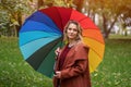 Beautiful young woman standing in the park under a rainbow colored umbrella. A beautiful girl walks through the autumn Royalty Free Stock Photo