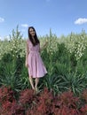 A beautiful young woman stands in the face of huge tall flowers.