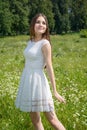 Beautiful young woman stands at a flowery meadow in a white dress Royalty Free Stock Photo