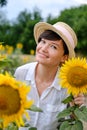 A beautiful young woman in a straw hat stands in a field of sunflowers.