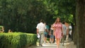 Beautiful young woman strolling in a park by herself at summertime while other people walking by her