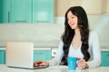 Beautiful young woman student freelancer in a white dress and black hair working at home with a laptop in a turquoise Royalty Free Stock Photo