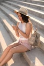 Beautiful young woman with stylish backpack and smartphone sitting on stairs outdoors Royalty Free Stock Photo