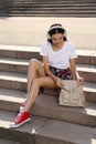 Beautiful young woman with stylish beige backpack and headphones on stairs outdoors Royalty Free Stock Photo