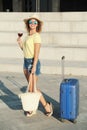 Beautiful young woman with suitcase and wine glass waiting a ship for summer trip. Curly hair happy woman with backpacks on the pi Royalty Free Stock Photo