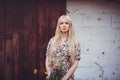 Beautiful young woman in a summer dress with wildflowers on a wall background with holes from bullets looking at the camera. aggre