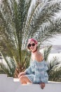 beautiful young woman in sunglasses and dress smiling at camera while sitting at resort Royalty Free Stock Photo