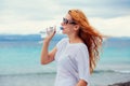 Beautiful young woman in sunglasses drinking water in summer beach outdoor with sea background Royalty Free Stock Photo