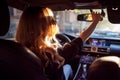 Beautiful young woman in sunglasses sitting behind the wheel of a car and corrects mirror. Photo from the back seat Royalty Free Stock Photo