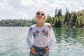 beautiful young woman in sunglasses standing near scenic tranquil mountain lake Royalty Free Stock Photo