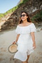 Beautiful young woman with sunglasses walks holding a hat on a beach Royalty Free Stock Photo