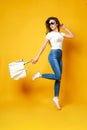 Beautiful young woman in sunglasses, white shirt, blue jeans jumping with bag on the yellow background Royalty Free Stock Photo