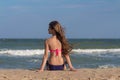 Beautiful young woman in a swimsuit with long hair sits on the beach near the sea Royalty Free Stock Photo