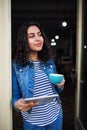 A beautiful young woman with tablet and coffee standing at the front door in cafe.