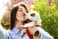 Beautiful young woman takes selfie of her kissing cute jack russell terrier puppy on picnic in park, green grass & foliage backgro Royalty Free Stock Photo