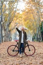 Beautiful young woman taking selfie with her smart phone while cycling through the park in autumn Royalty Free Stock Photo