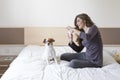 beautiful young woman taking a selfie with mobile phone on bed with her cute small dog besides. Home, indoors and lifestyle Royalty Free Stock Photo