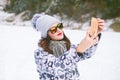 Beautiful young woman taking a selfie in winter nature. Pretty woman taking a photo in a nature. Winter background.