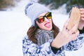 Beautiful young woman taking a selfie in winter nature. Pretty woman taking a photo in a nature. Winter background.