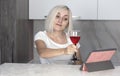 Beautiful young woman talking by video call via tablet, holding a glass of red wine Royalty Free Stock Photo