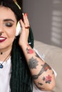 Beautiful young woman with tattoos on body, nose piercing and dreadlocks listening to music indoors, closeup Royalty Free Stock Photo