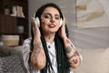 Beautiful young woman with tattoos on body, nose piercing and dreadlocks listening to music at home Royalty Free Stock Photo