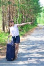 young woman tourist with a suitcase on a forest road on a summer sunny day against the backdrop of green trees. Close-up. Selecti Royalty Free Stock Photo