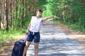 Beautiful young woman tourist with a suitcase on a forest road on a summer sunny day against the backdrop of green trees. Close-up Royalty Free Stock Photo