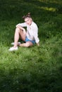Beautiful young woman in trendy casual clothes sitting on the grass