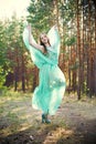 Beautiful young woman in a turquoise dress in a pine forest