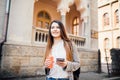 Beautiful young woman is using an app in her smartphone device to send a text message in front of a city background Royalty Free Stock Photo