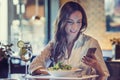 A beautiful young woman is using an application to send an sms message in her smartphone device while eating a salad at the restau Royalty Free Stock Photo