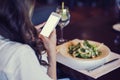 A beautiful young woman is using an application to send an sms message in her smartphone device while eating a salad at the restau Royalty Free Stock Photo
