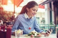 A beautiful young woman is using an application to send an sms message in her smartphone device while eating a salad at the restau Royalty Free Stock Photo