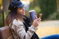 Beautiful young woman using her mobile phone while drinking coffee and sitting in a bench in the street Royalty Free Stock Photo