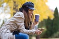 Beautiful young woman using her mobile phone while drinking coffee and sitting in a bench in the street Royalty Free Stock Photo