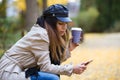 Beautiful young woman using her mobile phone while drinking coffee and sitting in a bench in the street. Royalty Free Stock Photo